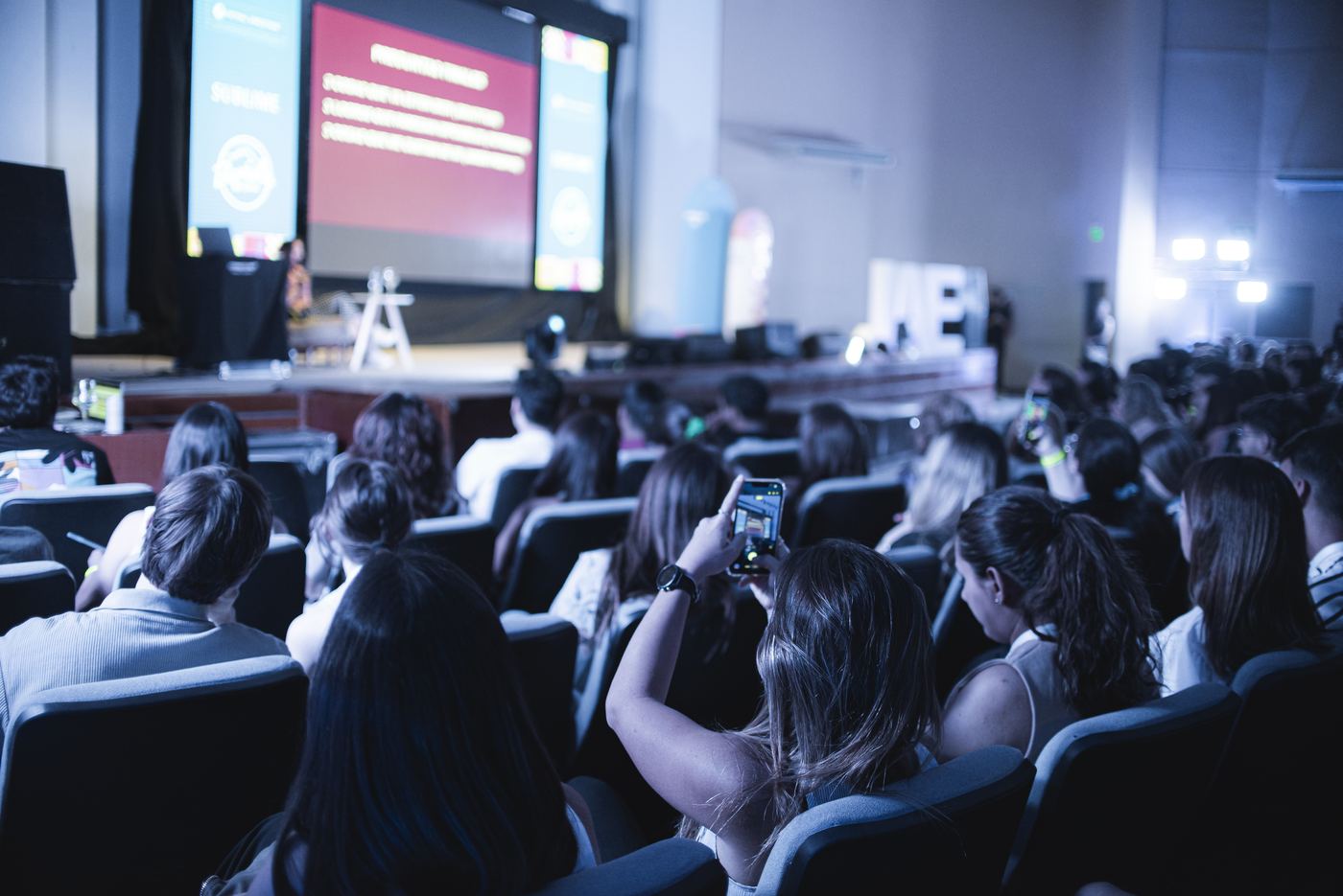 Asistentes filmando una charla desde sus butacas
